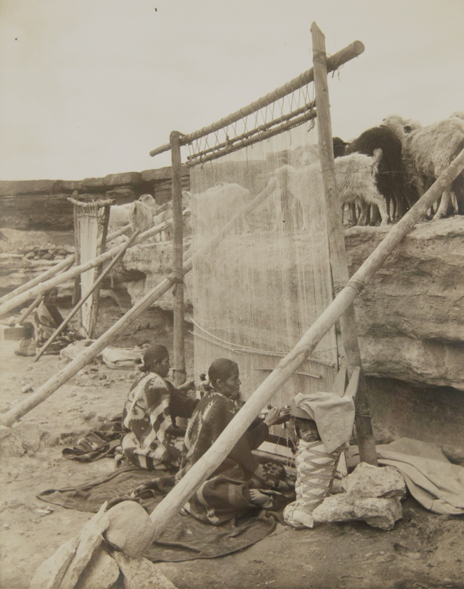 Navajo women surrounded by desert weave giant rugs below their sheep and goats